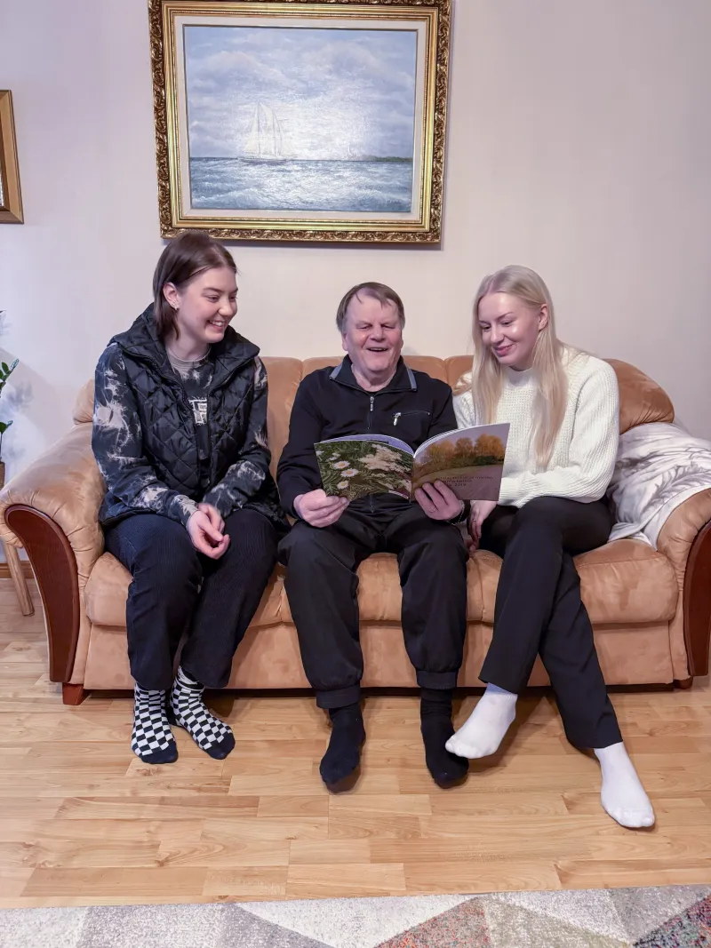 Helpen avustajat ja asiakas katsovat yhdessä lehteä sohvalla